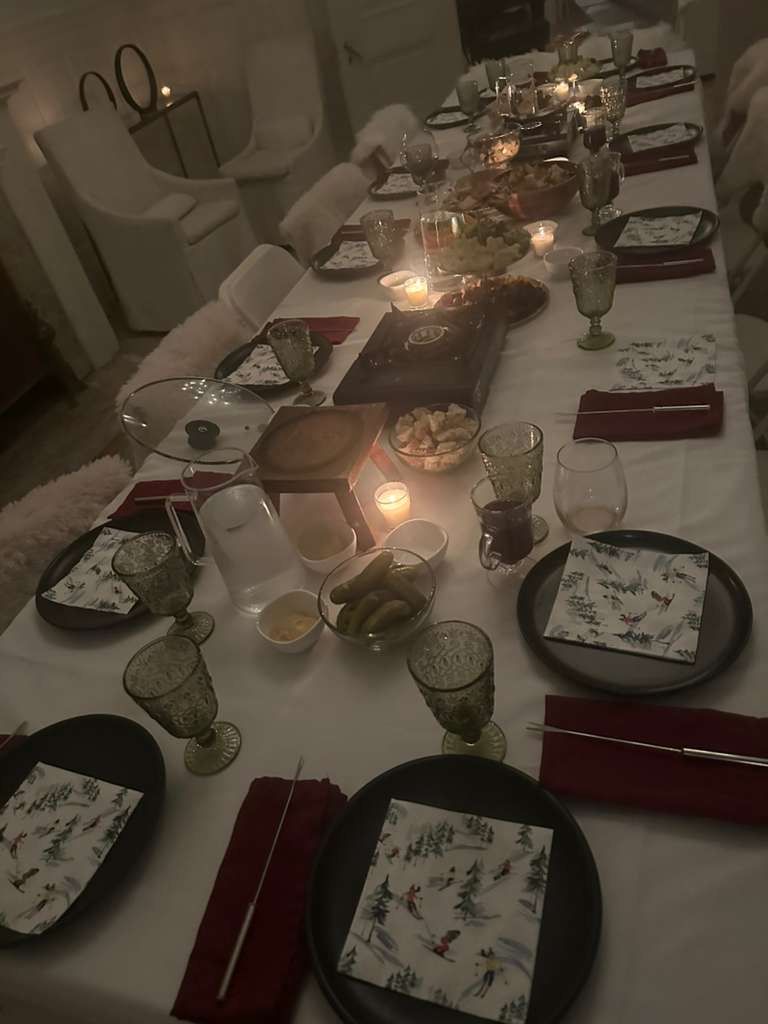 Close-up of the fondue dinner table — black plates, green goblets, ski-themed napkins, wooden boards, and fondue pots