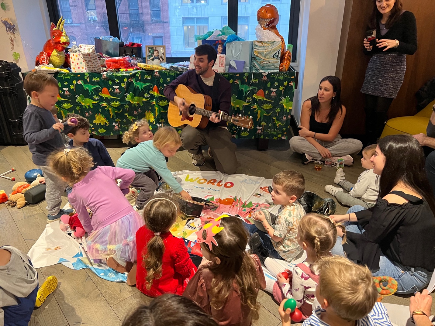 Mr. John performing guitar with kids sitting in a circle, world map on the floor