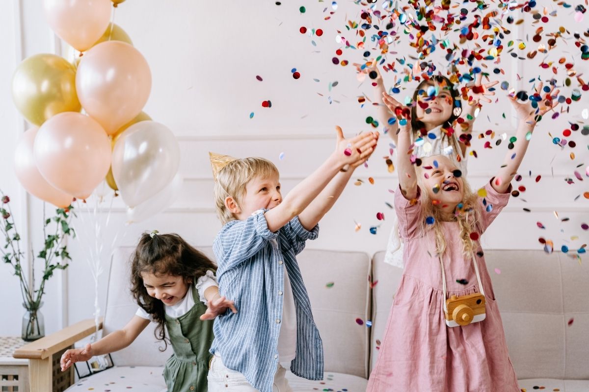 Kids throwing confetti at an apartment birthday party with balloons