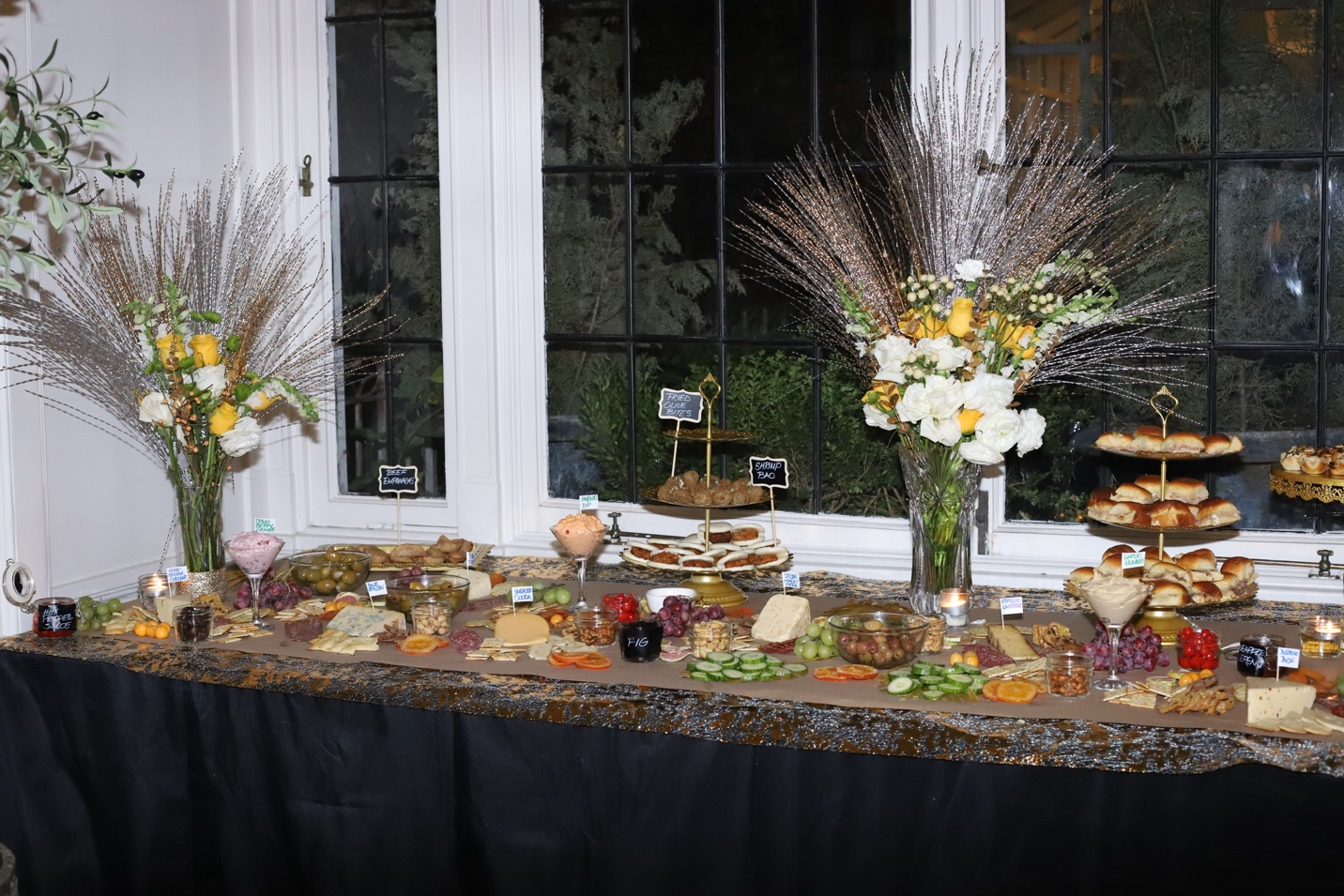 The full grazing table — kraft paper, charcuterie, tiered gold stands, flower arrangements, and chalkboard labels