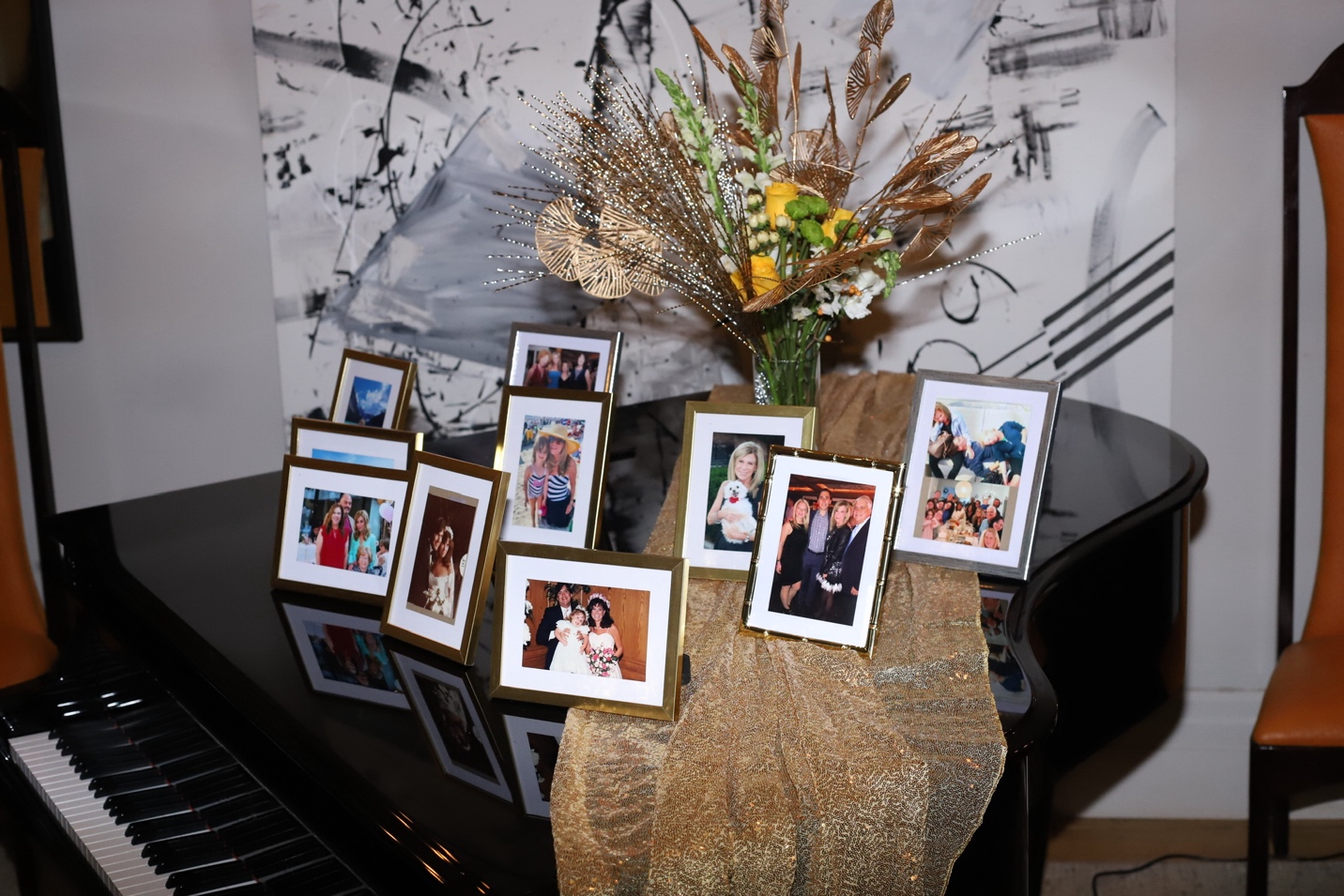 Gold-framed photos arranged on the grand piano with a dried flower arrangement and abstract painting behind