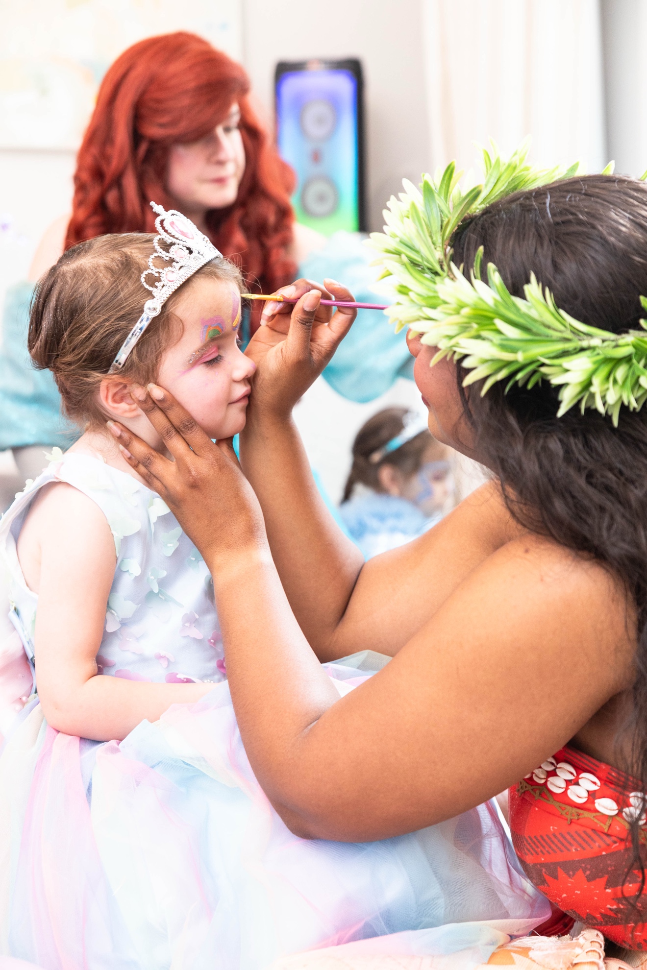 Moana painting a butterfly on Ellie's cheek while she wears her tiara