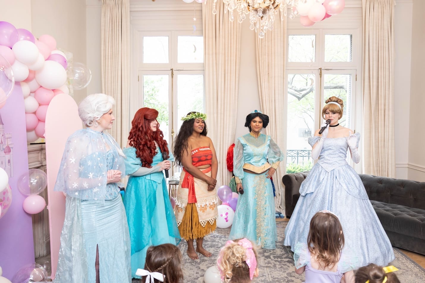Five princess performers — Elsa, Ariel, Moana, Jasmine, and Cinderella — performing for the children